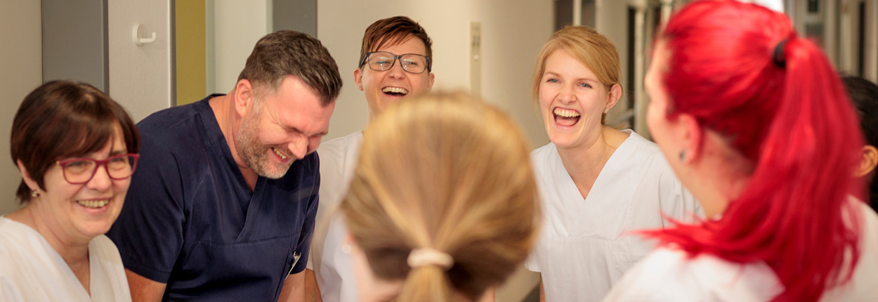Sechs Personen in weißen Arbeitskleidung stehen in einer Gruppe, einige blicken auf den Boden, andere nach vorne.